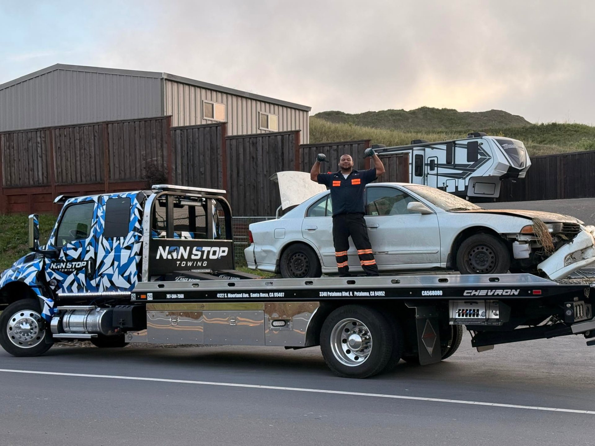 Non Stop Towing operator with a flatbed carrying a wrecked vehicle